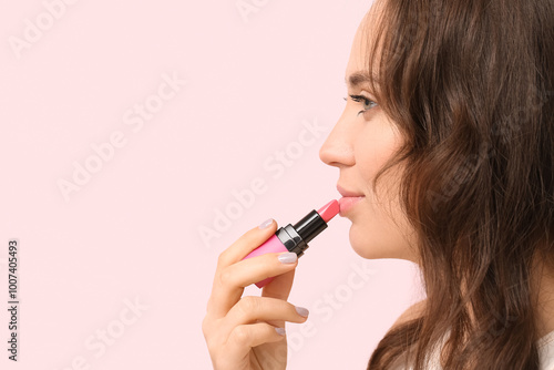 Beautiful young woman applying pink lipstick against color background, closeup