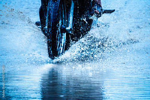 A motorcycle is riding through a puddle of water, creating a splash. Concept of excitement and adventure, as the rider navigates the wet road