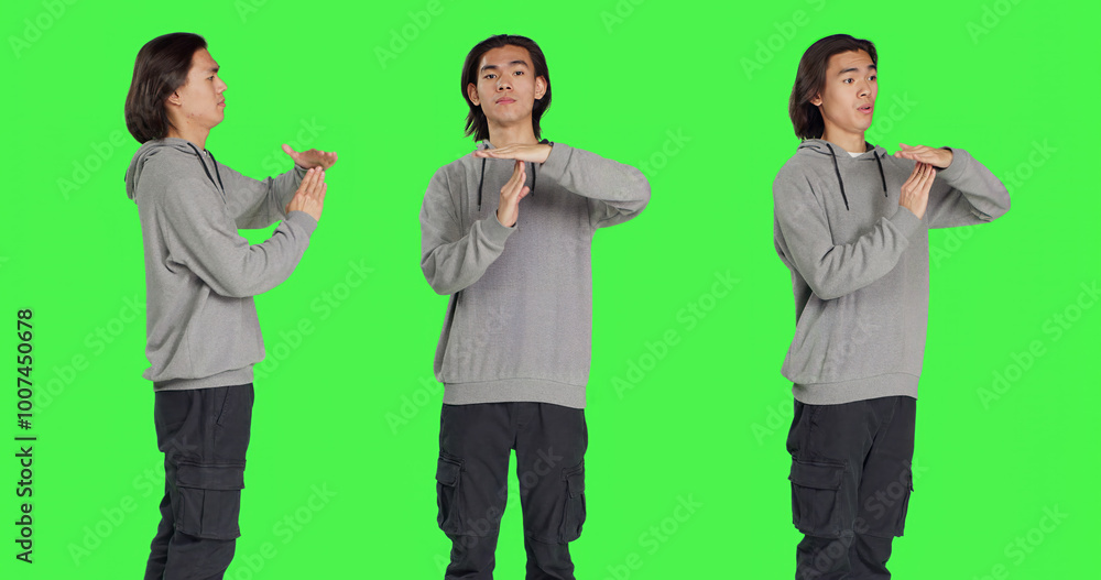 Person does timeout gesture with hands, asking for a break or pause against greenscreen in studio. Asian man showing disapproval and negative emotions on camera, stop gesture. Person does timeout gesture with hands, asking for a break or pause against greenscreen in studio. Asian man showing disapproval and negative emotions on camera, stop gesture.