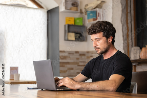 Freelance happy young man enjoying a delicious breakfast of latte and brouni in a specialty cafe, works with his laptop and smartphone, digital nomad, thoughtfully enjoys a cappuccino coffee