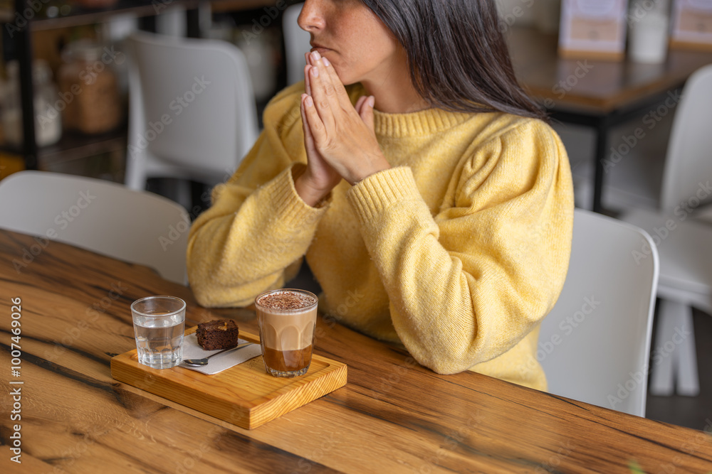 Happy young woman smiling enjoys her breakfast or lunch recovering energy with a delicious caramel coffee and eats a chocolate cupcake, close-up in a specialized pastry cafe on wooden table Happy young woman smiling enjoys her breakfast or lunch recovering energy with a delicious caramel coffee and eats a chocolate cupcake, close-up in a specialized pastry cafe on wooden table
