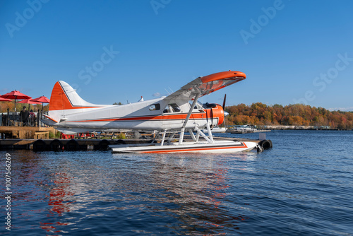 Close view of small private seaplane parked at Georgian Bay by wooden pier at outdoor restaurant patio. Sunny clear fall day, blue sky.