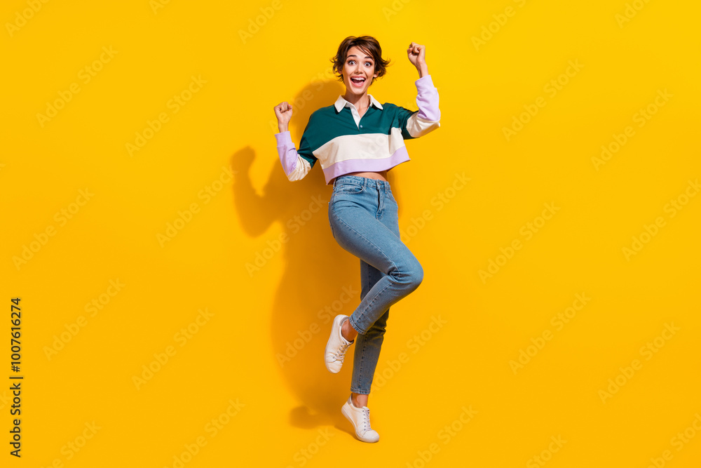Full length photo of pretty lucky woman wear polo shirt rising fists isolated yellow color background Full length photo of pretty lucky woman wear polo shirt rising fists isolated yellow color background