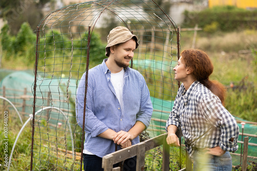 Guy and woman, peasant neighbors, met near arched trellis, talk and communicate, discuss news, exchange experiences.