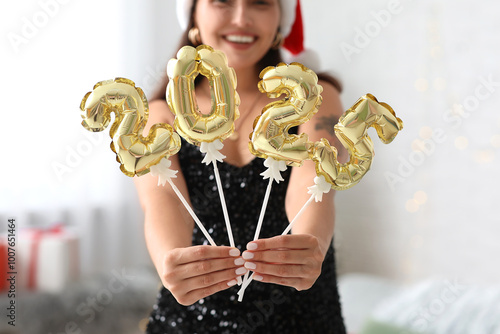 Beautiful young woman with figure 2025 made of foil balloons in living room. Christmas celebration