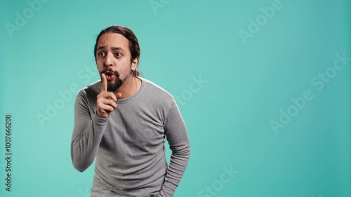 Portrait of man doing shushing hand gesturing, requesting silence. Person placing finger on lips, doing quiet sign gesture, asking for secrecy, isolated over studio background, camera B photo