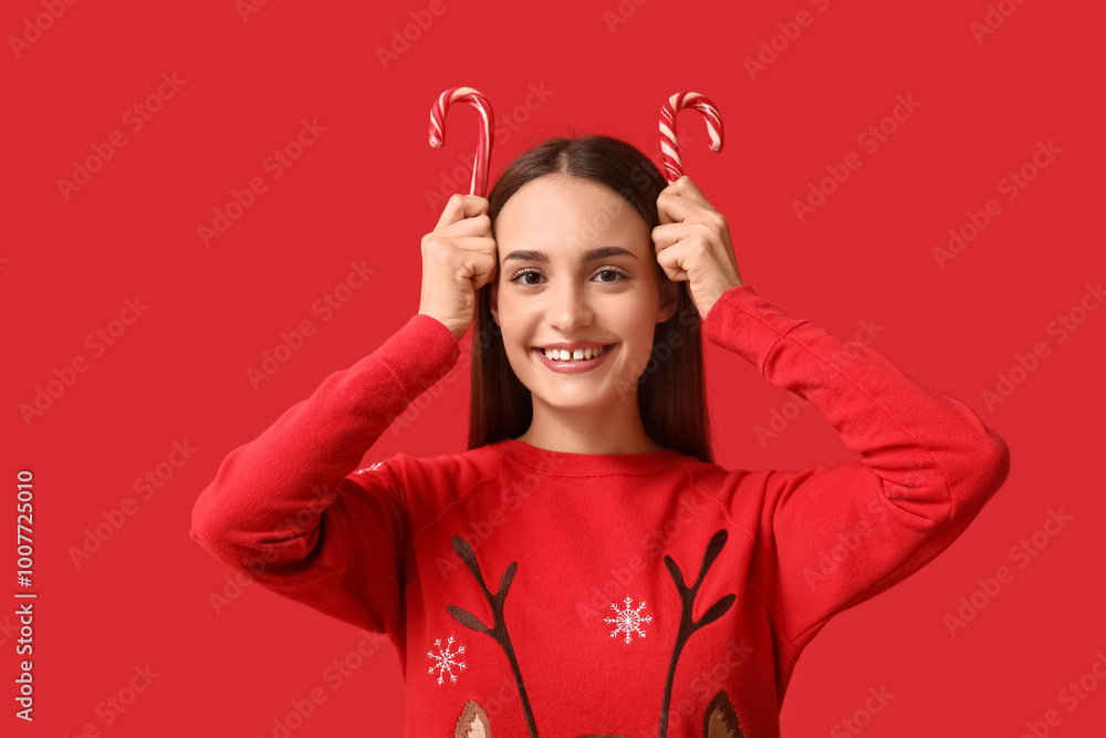Young woman in Christmas sweater with candy canes on red background Young woman in Christmas sweater with candy canes on red background
