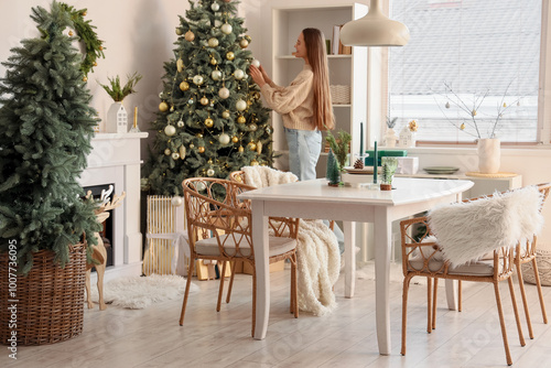 Young woman decorating Christmas tree in dining room