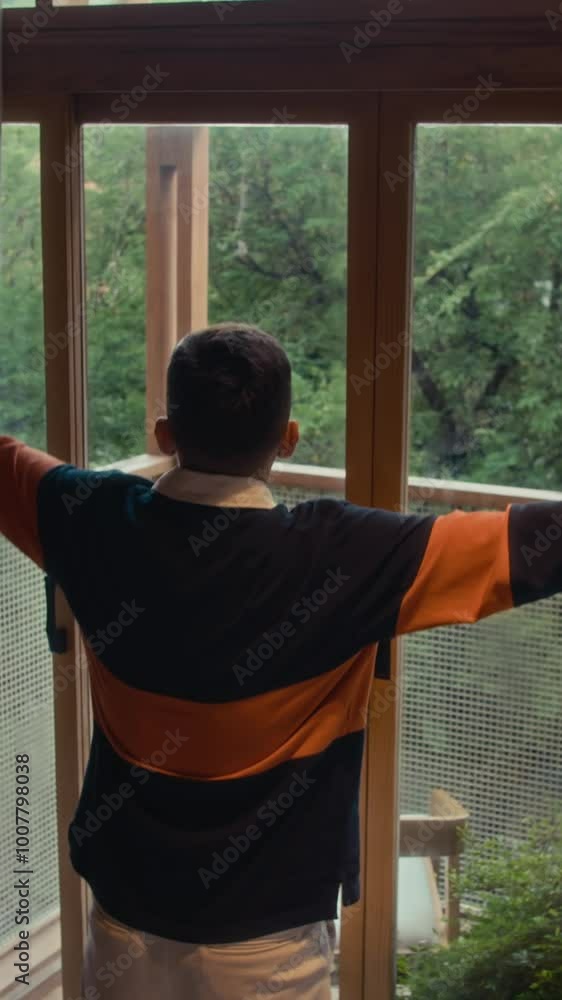 Vertical shot of Caucasian man getting up and stretching by panoramic window at home Vertical shot of Caucasian man getting up and stretching by panoramic window at home