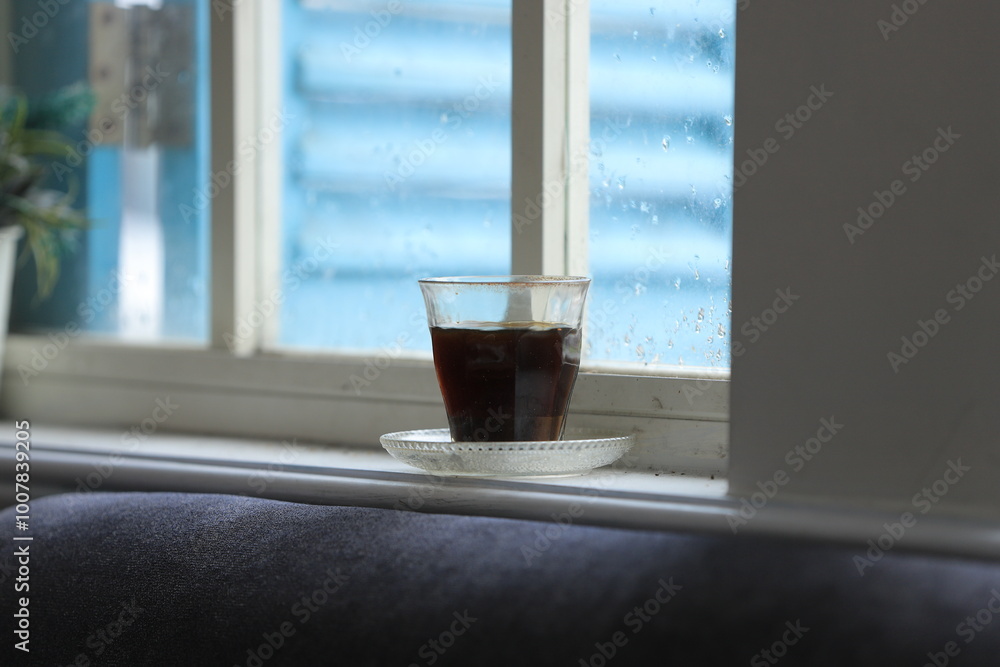 A glass of black coffee on the Window Sill, with against the warm light from the sunny day outside. A glass of black coffee on the Window Sill, with against the warm light from the sunny day outside.