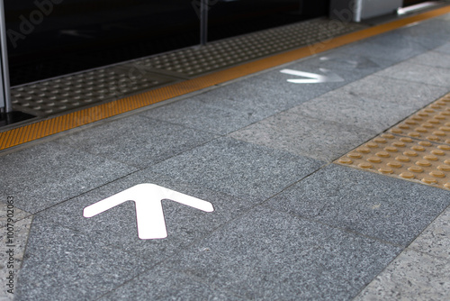 Subway platform arrow sign indicating direction entrance and exit on textured floor at train station.