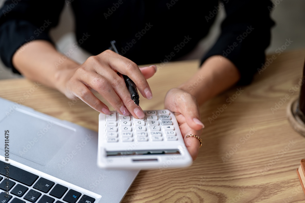 A close-up of a businesswoman's hand holding and using a calculator, focused on her work. A close-up of a businesswoman's hand holding and using a calculator, focused on her work.