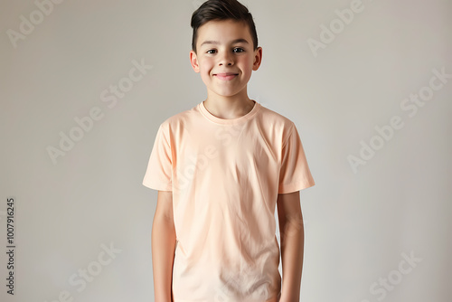 A young Hispanic boy poses cheerfully in a light peach t-shirt, exuding joy and confidence against a soft gray background.