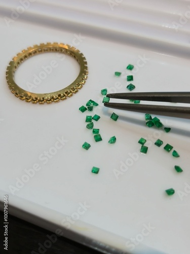 loose stones as emerald for choosing making ring. there is a gold ring setting on white paper background. Photo for jewelry store marketing