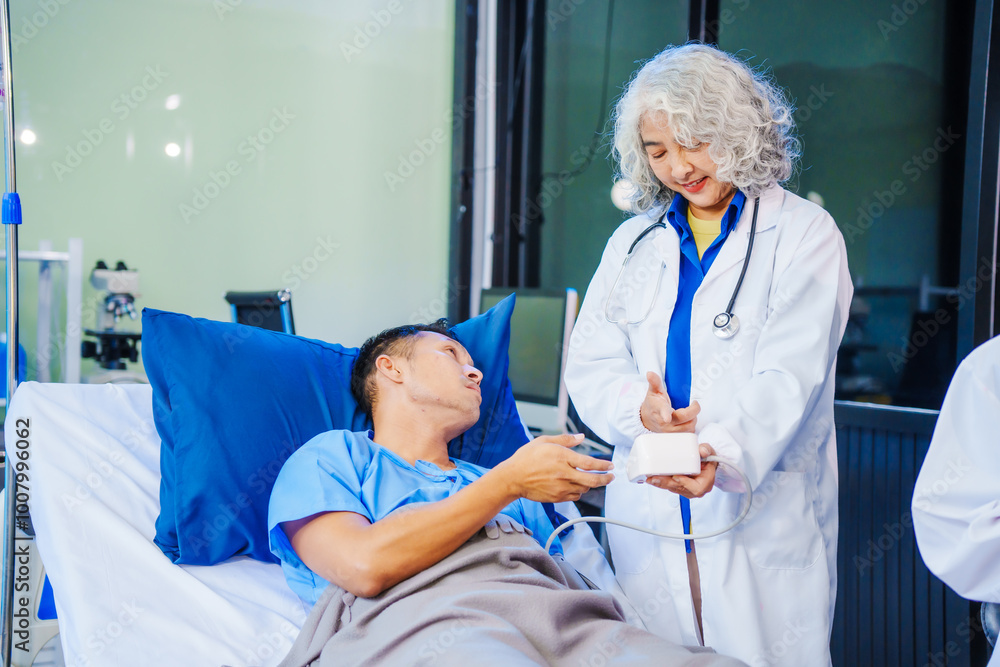 A middle-aged man lies bedridden on hospital bed, closely monitored by an old Asian woman doctor and young nurse. They assess his symptoms, including heart and lung conditions, offer advice. A middle-aged man lies bedridden on hospital bed, closely monitored by an old Asian woman doctor and young nurse. They assess his symptoms, including heart and lung conditions, offer advice.