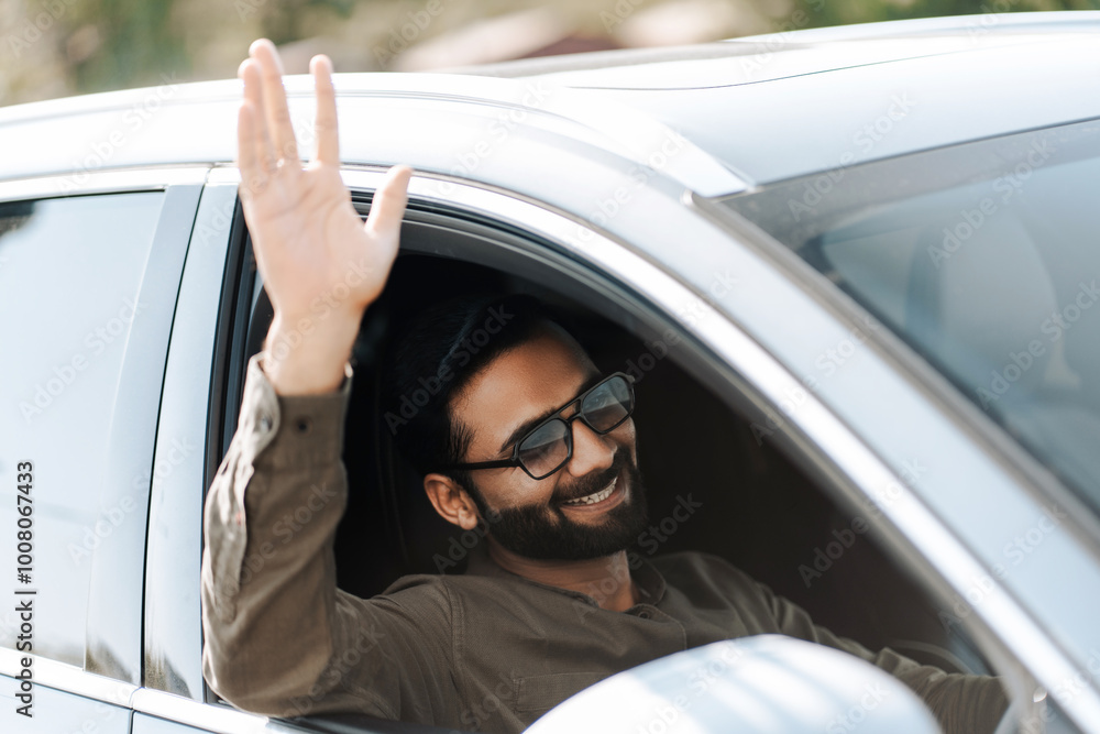 Happy Indian businessman waving from car window, driving on the street Happy Indian businessman waving from car window, driving on the street