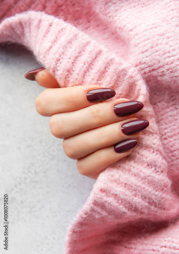 Obraz na płótnie Elegant woman's hand with deep burgundy nails holding a soft pink sweater against a textured background w salonie