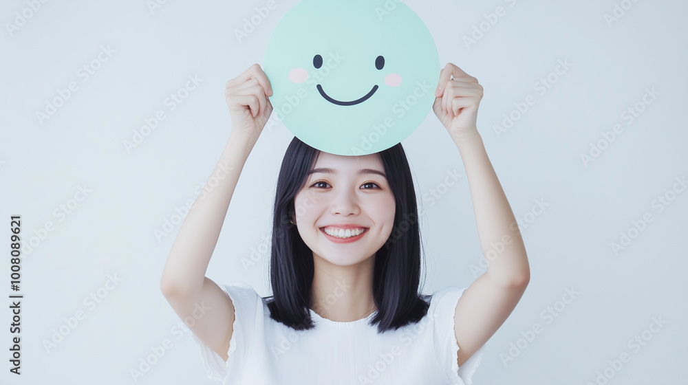 Happy Asian girl holding a smile emoji face, positive mental health concept Happy Asian girl holding a smile emoji face, positive mental health concept