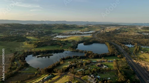 Aerial dolly establishes Minnamurra, Australia, featuring coastal landscapes and ponds with a beautiful clear sky above lush town photo