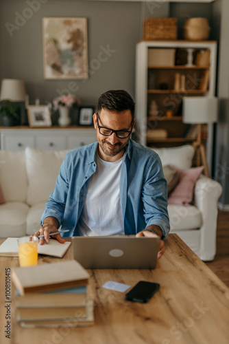 A focused male writer and businessman typing on his laptop while sitting at a table at cozy home