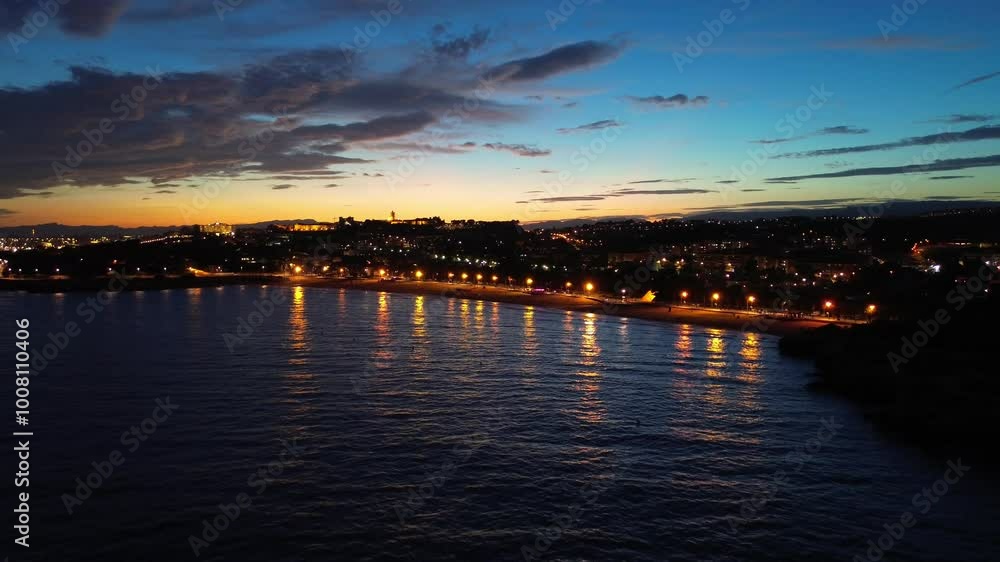 Playa de l'arrabassada at dusk with streetlights illuminating the shoreline, aerial view Playa de l'arrabassada at dusk with streetlights illuminating the shoreline, aerial view