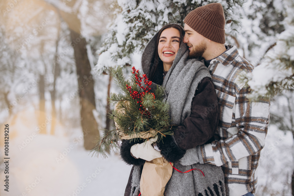 Fototapeta premium Cute young couple in love with pine bouquet spending time on Valentine's day in snowy winter forest in mountains