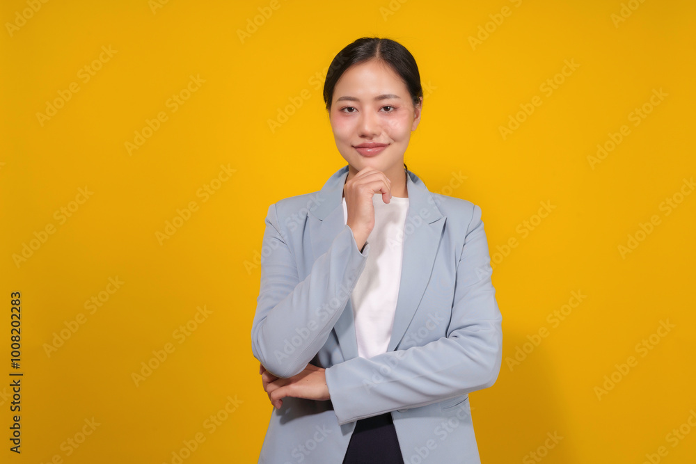 Young professional woman is posing on a yellow background, touching her chin with a confident smile Young professional woman is posing on a yellow background, touching her chin with a confident smile