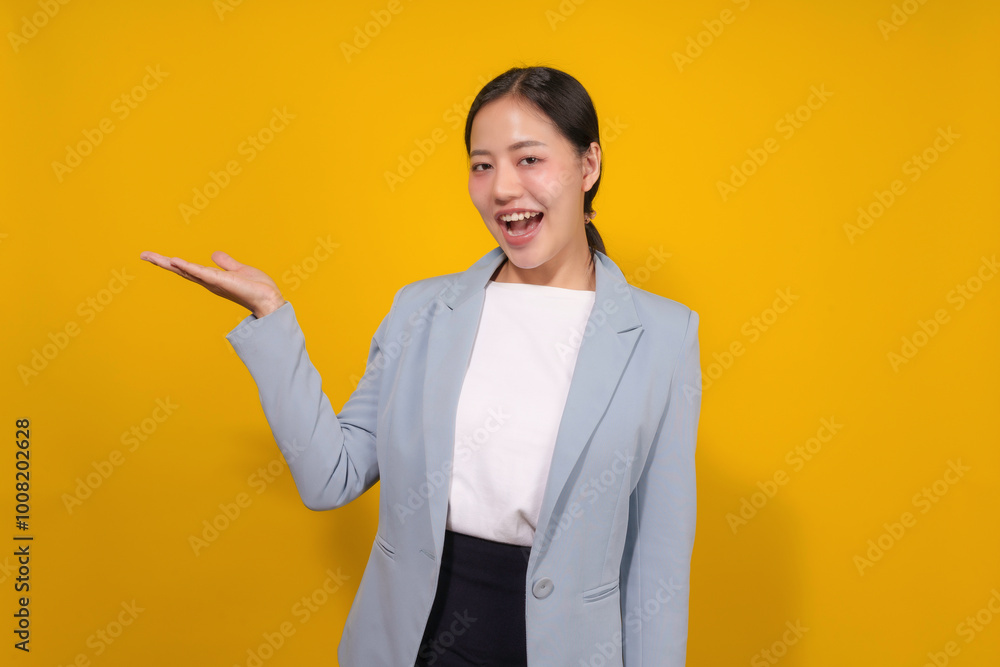 Asian businesswoman wearing a blue blazer is gesturing with her hand and smiling on a yellow background Asian businesswoman wearing a blue blazer is gesturing with her hand and smiling on a yellow background
