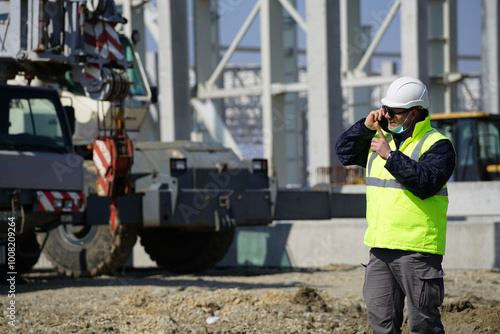 Portrait of young architect with reflective clothing on construction site and with a mask and excavator on the background 