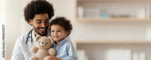 A doctor is wearing a white coat and has a stethoscope around his neck, sitting with a happy child in a medical office