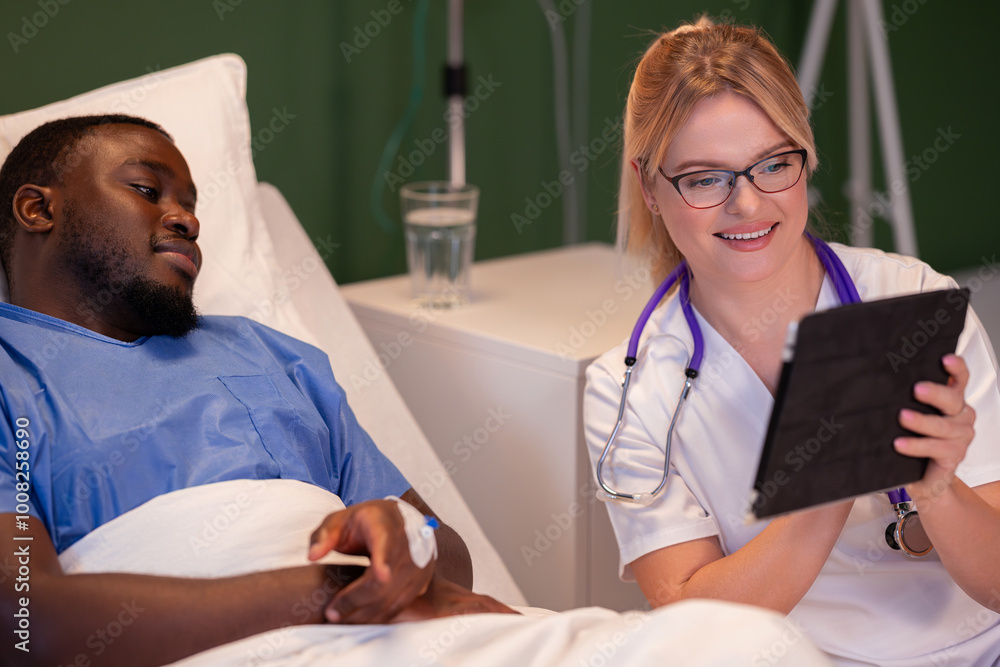 Fototapeta premium Holding a tablet, the doctor looks at the patient's information while sitting beside them.