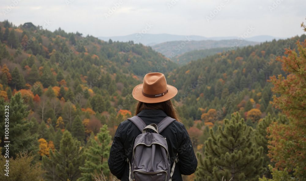 A woman is hiking in the mountains, standing on a hill overlooking a valley with stunning autumn foliage. She is wearing a brown hat and a backpack and looking out at the autumn view A woman is hiking in the mountains, standing on a hill overlooking a valley with stunning autumn foliage. She is wearing a brown hat and a backpack and looking out at the autumn view
