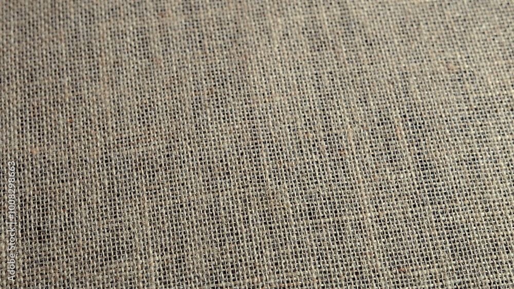 Textured burlap fabric reveals rough fibers in close-up view. Light enhances handcrafted woven design, highlighting rustic aesthetic and natural imperfections. Textured burlap fabric reveals rough fibers in close-up view. Light enhances handcrafted woven design, highlighting rustic aesthetic and natural imperfections.