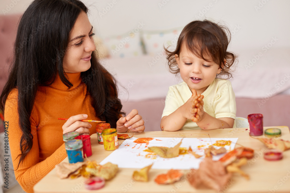 happy little child girl and mom spending good time painting hands and autumn yellow leaves together happy little child girl and mom spending good time painting hands and autumn yellow leaves together