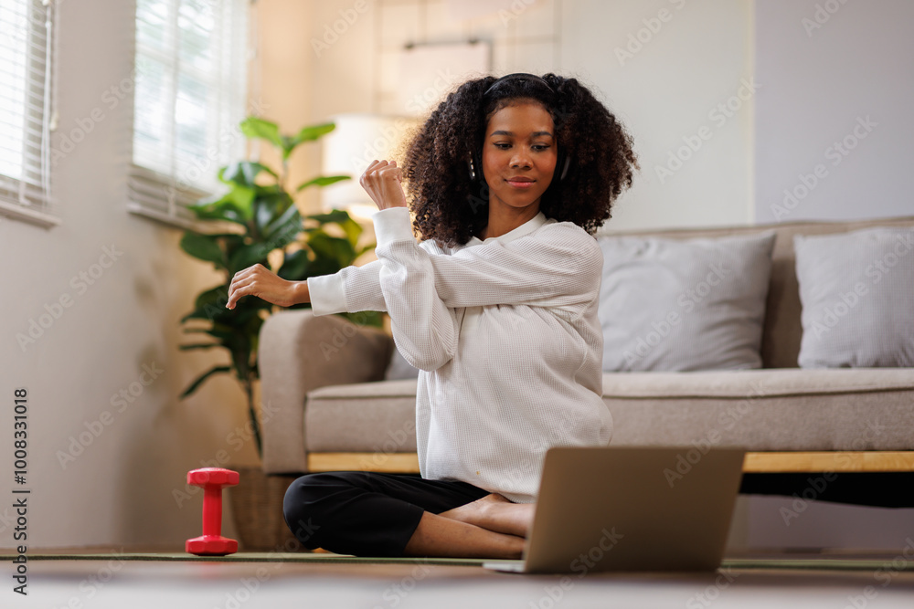 A curly African American woman in activewear practices yoga in a serene living room Meditating at Home with Headphones setting.
