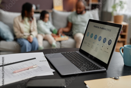 Family sitting on couch engaging in financial planning activity visible on laptop screen on table foreground. Parents and kids interacting, discussing important financial information