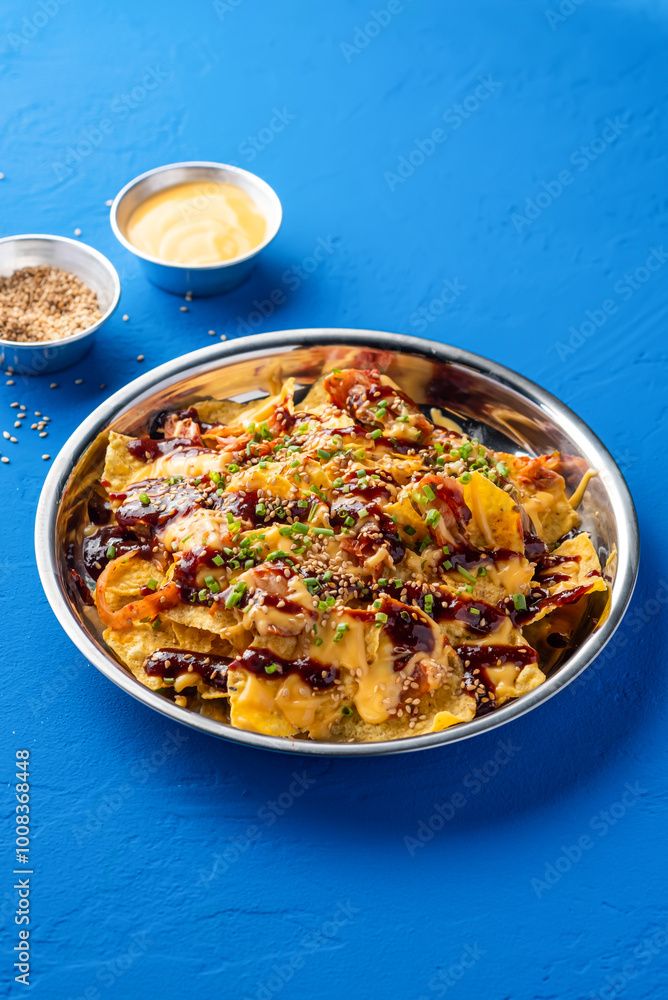 Loaded Fries Nachos with Kimchi, Chicken, Cheese, Sauce, Mayonnaise dip, sesame seeds and green onion served in plate isolated on blue background closeup side view of fast food Loaded Fries Nachos with Kimchi, Chicken, Cheese, Sauce, Mayonnaise dip, sesame seeds and green onion served in plate isolated on blue background closeup side view of fast food