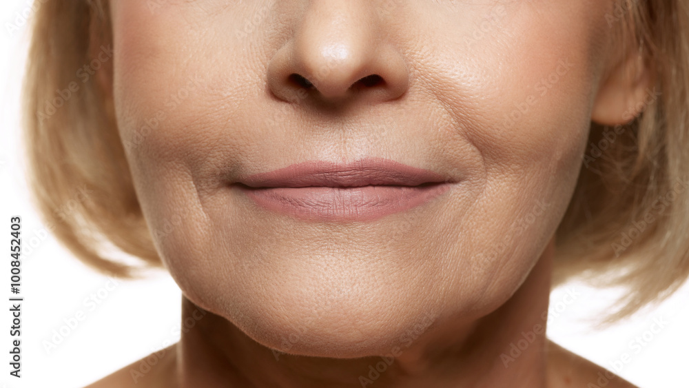 Obraz premium Extremely close-up of smiling woman, showcasing natural lips and fine lines with glowing skin against white studio background. Concept of beauty, wellness, cosmetology, anti-aging products. Ad