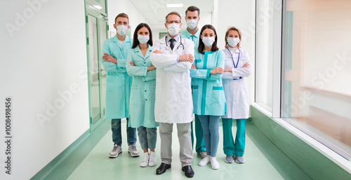 Group of masked healthcare professionals, standing confidently in hospital hallway, showcasing safety, teamwork, and professionalism during medical crisis. Healthcare and pandemic-related themes photo