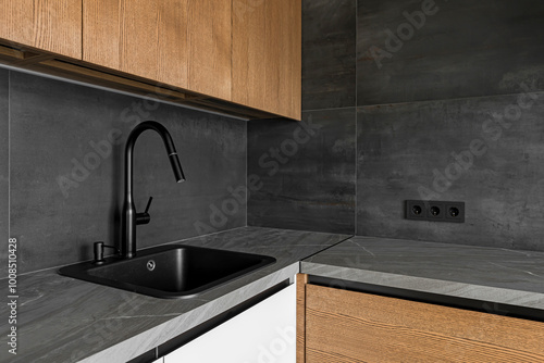 Dark grey kitchen table top, sink with water tap, against a dark grey tiled wall