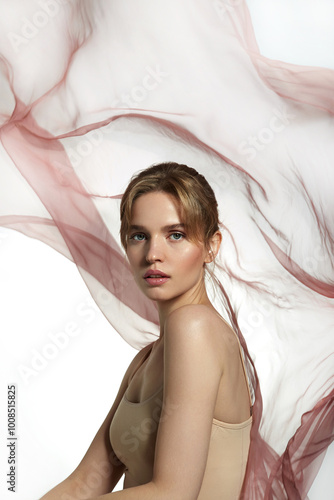 Portrait of a beautiful young woman with natural makeup and smooth skin, against the background of soft flowing fabric. The image emphasizes tenderness and lightness, creating a romantic mood. 