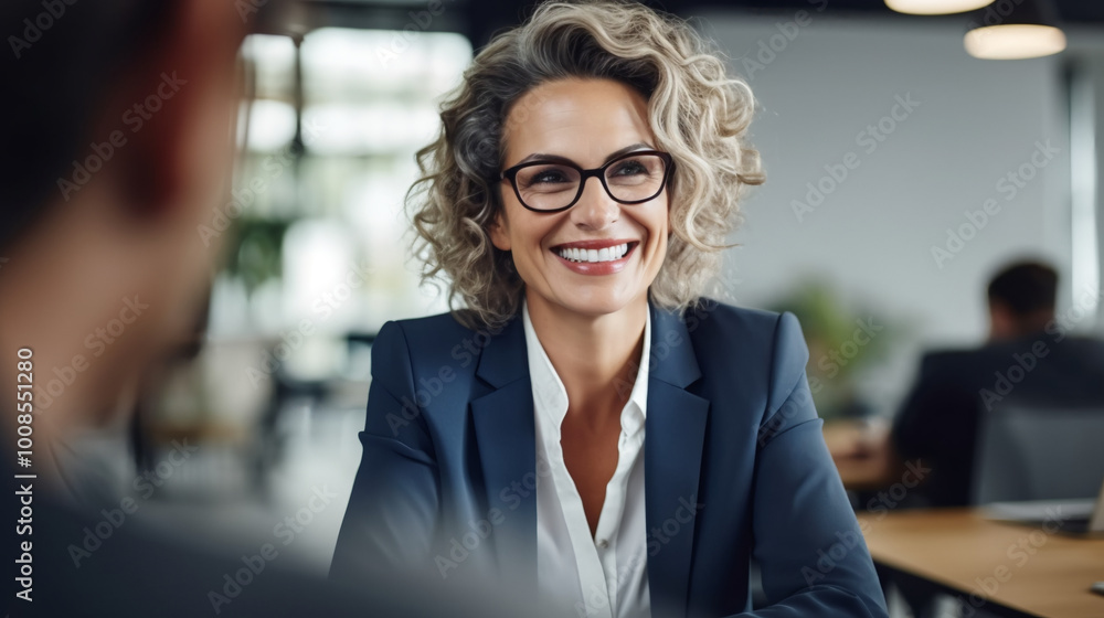 photograph of an attractive, smiling businesswoman wearing glasses, sitting in the office during a meeting, and talking to other people. photograph of an attractive, smiling businesswoman wearing glasses, sitting in the office during a meeting, and talking to other people.
