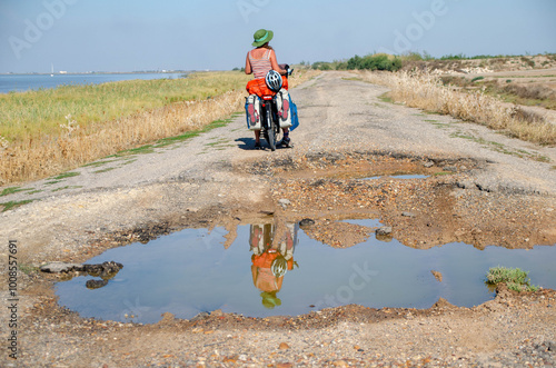 Woman riding alone on a bicycle on broken and pot-holed roads discovering natural environments. 