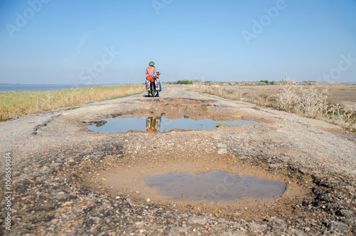 Woman riding alone on a bicycle on broken and pot-holed roads discovering natural environments. 