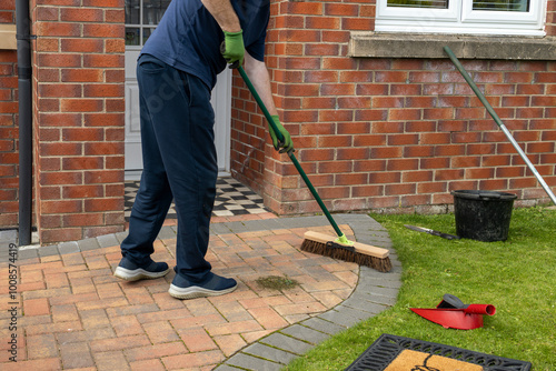 Принти на полотні Man sweeping a brick driveway path in front of a house with bucket, broom, and o