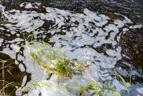 River with white foam caused by pollution or sewage runoff into water with grass at edge of stream photo