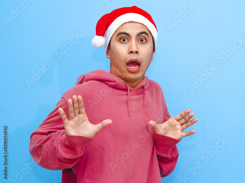 Portrait of a young Asian man wearing a red hoodie and Santa hat with a funny shocked expression. Perfect for Christmas and New Year's advertising. photo