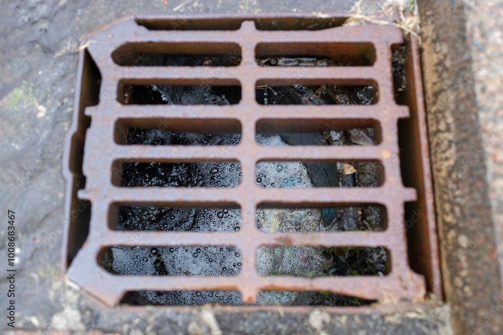 Rusty storm drain grate with rain water and debris flowing through with foamy bubbles