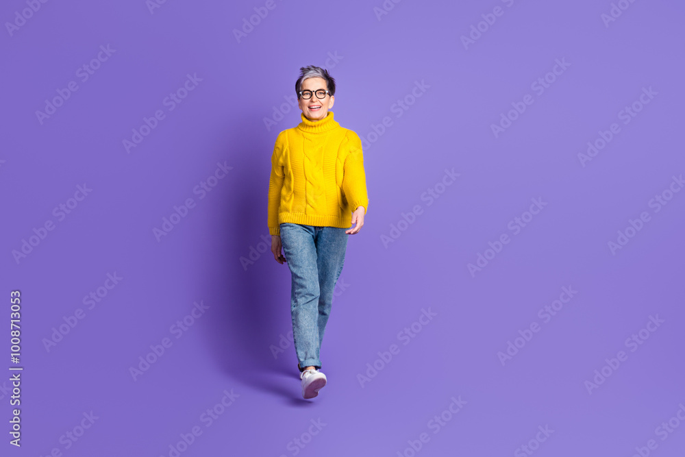 Full length photo of adorable funny woman yellow knitwear smiling walking empty space isolated violet color background Full length photo of adorable funny woman yellow knitwear smiling walking empty space isolated violet color background