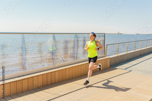 A Woman Jogging Along the Waterfront Promenade Under Clear Skies During a Sunny Morning in a Coastal Location